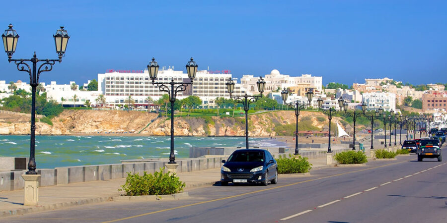 Qurum Beach in Muscat with palm trees, sandy shoreline, and residential buildings in the background.